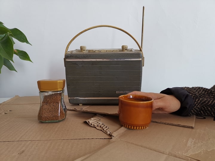 One hand is close to a cup of coffee. Behind it is a small radio.